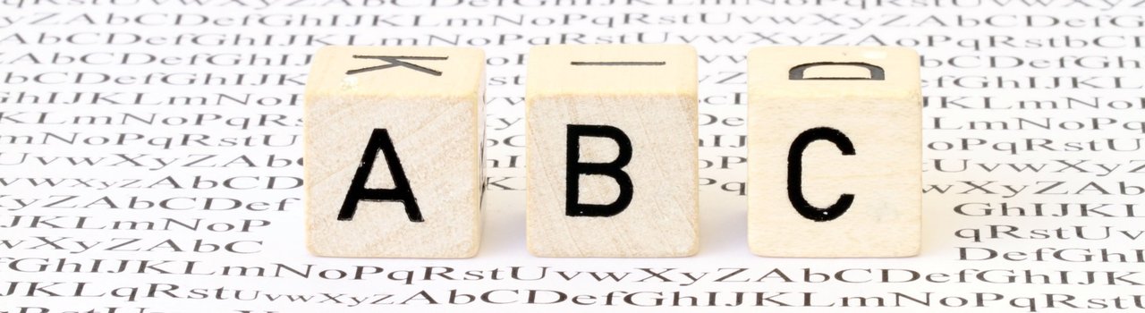 Headerbild Glossar zeigt Buchstabenwürfel ABC auf einem Papierbogen mit zahlreichen Buchstaben darauf