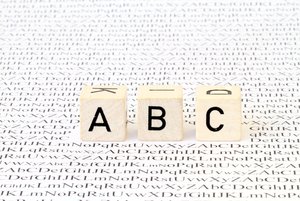 Headerbild Glossar zeigt Buchstabenwürfel ABC auf einem Papierbogen mit zahlreichen Buchstaben darauf